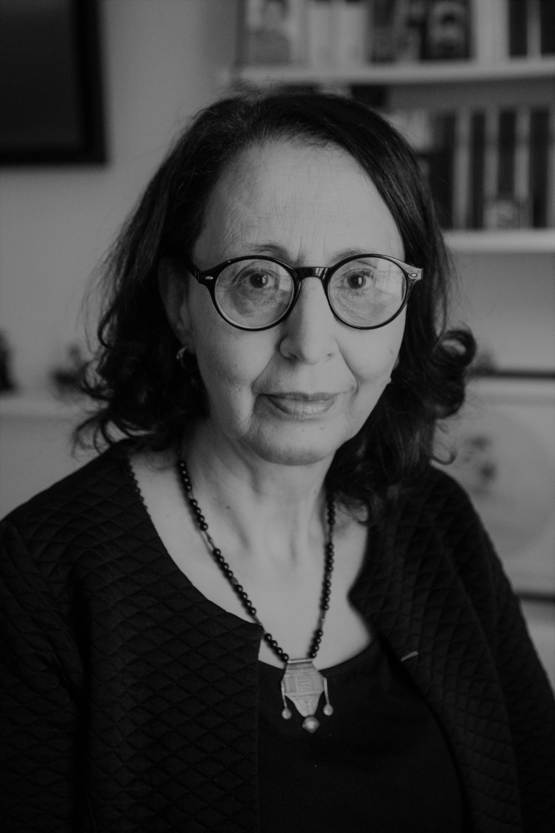 Portrait en noir et blanc de Fatima Besnaci-Lancou, historienne, aux cheveux mi-longs et portant des lunettes, souriant face à l'objectif